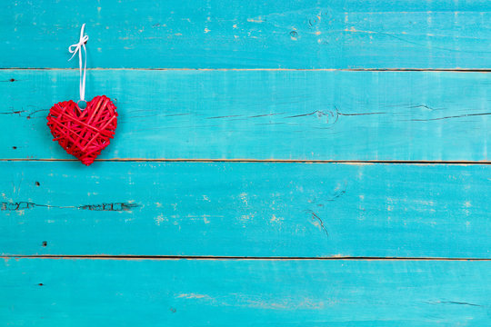 Red wicker heart hanging on blank antique teal blue wood sign; wooden background with copy space