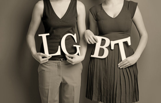 Young lesbian couple holding letters LGBT on color background