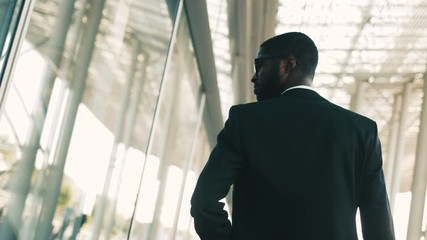 Confident african american businessman walking along big office windows outdoors. Back view. Shot from back. Close up - Powered by Adobe