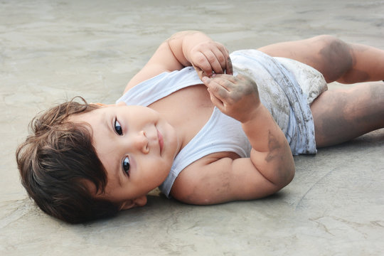 Happy dirty baby boy lying on muddy floor