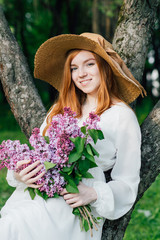 Redhead girl with a bouquet of lilacs in a spring garden