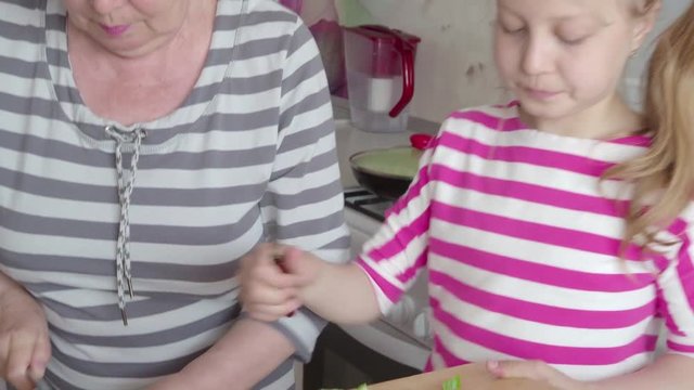 An elderly woman and a girl of 9 years together prepare a vegetable salad on the kitchen table. 4K