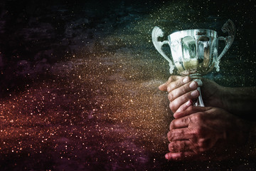 low key image of a man holding a trophy cup over dark background