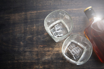 Glass with ice cubes and whiskey bottle on wooden table,top view