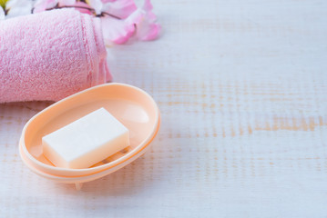 Pink rolled towel with soaps and flowers on white wood background.