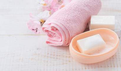 Obraz na płótnie Canvas Pink rolled towel with soaps and flowers on white wood background.