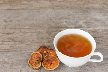 Ready to drink hot bael juice placed beside the bael fruit dried sliced into thin pieces on the wooden floor.
