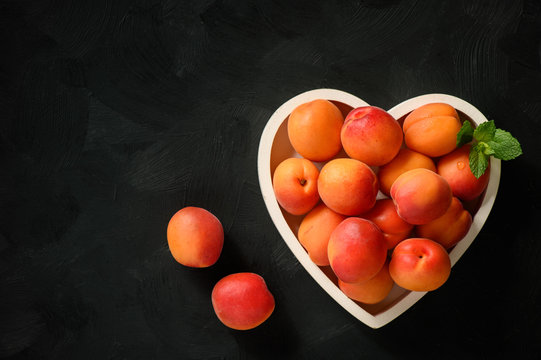Ripe apricots on wooden white tray on black background.