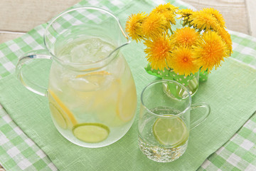 A jug of water and lemon and lime and a bouquet of dandelions
