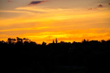 Orange sunset over silhouettes of village and trees
