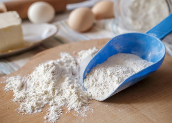 Wheat flour in blue plastic spoon on wooden board
