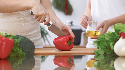 Close-up of four human hands are cooking in a kitchen. Friends having fun while preparing fresh salad. Vegetarian, healthy meal and friendship concept