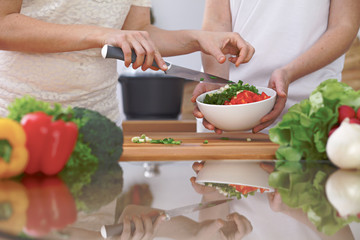Close-up of four human hands are cooking in a kitchen. Friends having fun while preparing fresh salad. Vegetarian, healthy meal and friendship concept