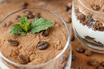 Two glasses with tiramisu, coffee beans and mint leaves. Dark background. Selective focus.