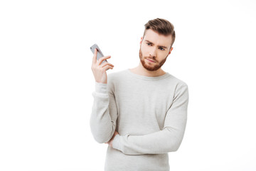 Annoyed young man holding smartphone far from his ear. Angry man doesn't want to listen talking on the phone isolated