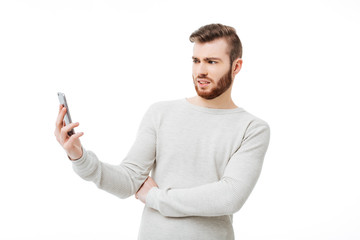 Young angry man looking with disgust on his smartphone isolated. Casual guy holding smartphone on his outstretched hand