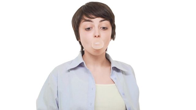 Young smiling Caucasian girl with short haircut chewing gum and blowing bubble over white background in slowmotion