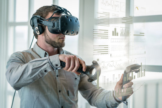 A businessman wearing a virtual reality headset, interacts with data.