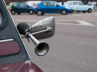 Closeup of klaxon attached to side mirror of vintage car. Black and white image.