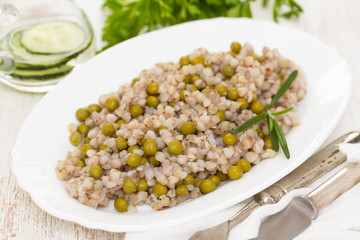 buckwheat with peas on white dish on wooden background