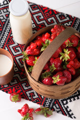 Strawberry in a bast basket and milk in a mug and a bottle on  a napkin with the Ukrainian ornament.
