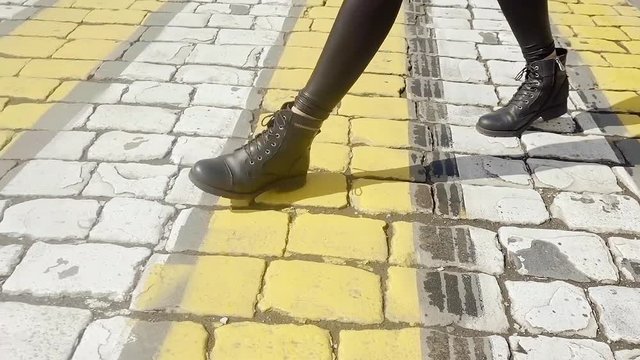 Female feet in heavy leather boots go on the road of stone with a painted Zebra for the transition.