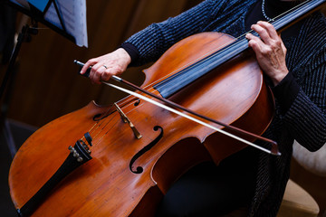 A young girl plays the cello in the dark. Hands on cello