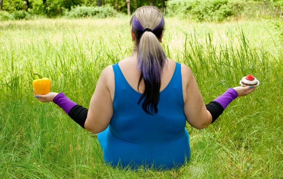 Fat woman wants to lose weight diet view from behind sits on grass image man figure in blue suit bush tree holds in hands choice in left hand yellow sweet bell pepper in right hand cake, torso purple 