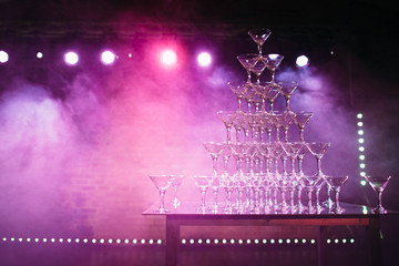 the pyramid of glasses with champagne on the wedding party. The smoke and light show. Background holiday themes