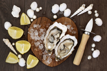 Fresh oysters on crushed ice on a heart shaped board with pearls, lemon fruit, oyster knife and shells on old oak background. High in omega 3 and protein.