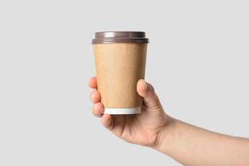 Mockup of male hand  holding a Coffee paper cup isolated on light grey background.
