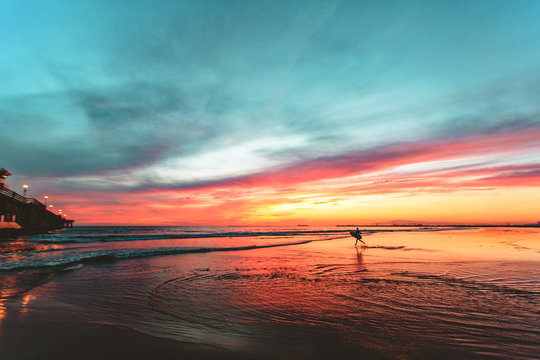 Surfer running on the beach during sunset