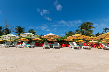 Colorful umbrella and beach chair on tropical beach with coconut trees and blue sky, vacation concept
