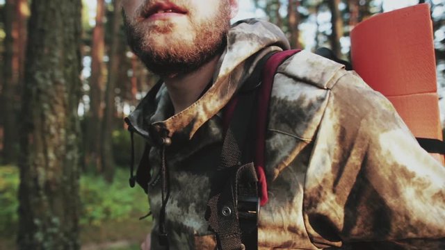 Close-up view of man with beard standing in the forest in the morning. Male in camouflage with backpack at nature.