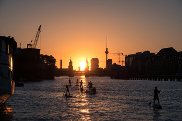 Obraz premium Niebo zachodzącego słońca Berlin Panorama - rzeka Spree, most Oberbaum, wieża telewizyjna i ludzie na desce do wiosłowania