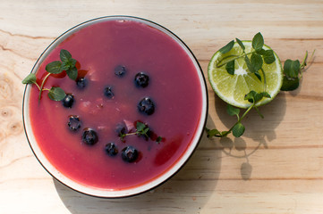 Blueberry fresh fruit smoothie bowl on wood with fresh lime and mint garnish