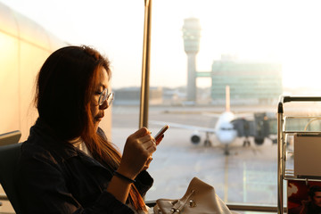 woman who wearing glasses is looking at smart phone at airport with playful face