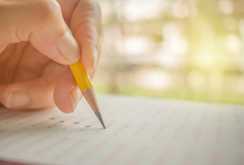 hand student testing in exercise and fill in exam carbon paper computer sheet with yellow pencil, education concept