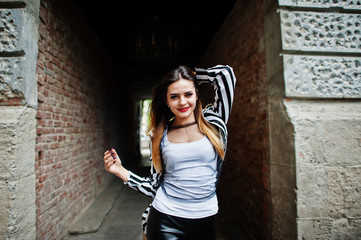 Fototapeta na wymiar Fashionable woman look with black and white striped suit jacket, leather pants, posing at old street red brick tunnel. Concept of fashion girl.