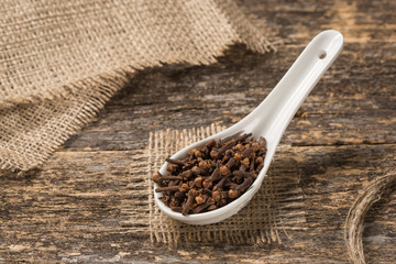 Porcelain spoon full of spices rests on old boards, rustic style, Spice cloves