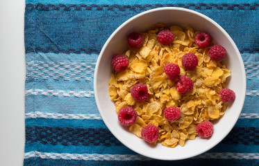 Breakfast cereal of cornflakes and raspberries on blue cloth background