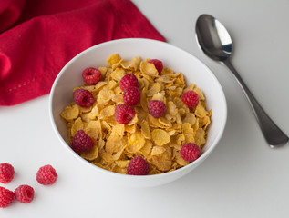 Cornflakes breakfast cereal with raspberries in bowl on white table