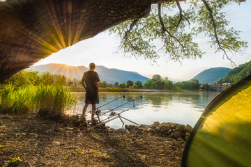 Angelabenteuer, Karpfenangeln. Angler fischt bei Sonnenuntergang mit Karpfenfischerei. Camping am Seeufer