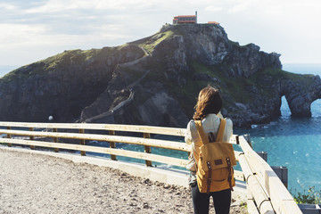 Hipster young girl with backpack enjoying sunset on seascape on peak mountain. Tourist traveler on...