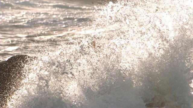 Surfer standing on rocks with wave crash in slow motion