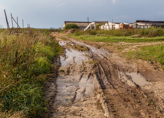A country road with ruts and mud leading to an farm