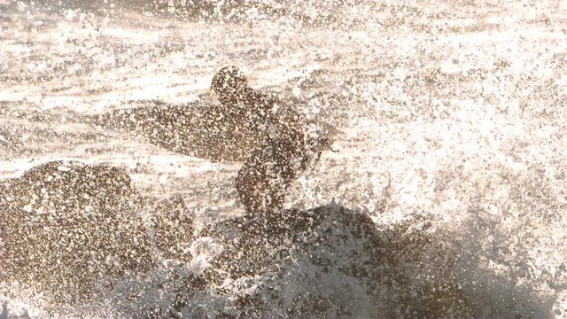Surfer on the rocks with slow motion wave crash