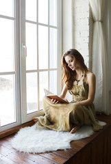 Beautiful woman sitting at a window and reading book