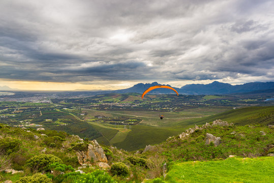 Paraglider flying over the green mountains around Cape Town, South Africa. Winter season, cloudy and dramatic sky. Unrecognizable people.