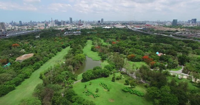 4K aerial shot of public park in Bangkok, Thailand in the morning with buildings.